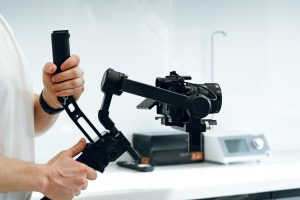 A person operates a handheld gimbal stabilizer with a camera in a modern studio setting during a