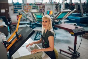 Portrait of print shop worker using heating press on textile product.